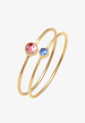 To tynde guldringe med kantsatte runde ædelsten, en lyserød og en blå, vist på en hvid baggrund.