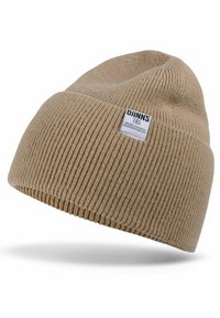 Beige knit beanie with ribbed texture. Features a small white label with black text. The design is soft and stretchy, suitable for cold weather.