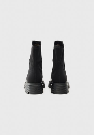 Botas negras hasta el tobillo, fabricadas en material sintético suave; cuentan con una suela texturizada y un diseño de costuras mínimas. Caña alta con puntera redondeada.