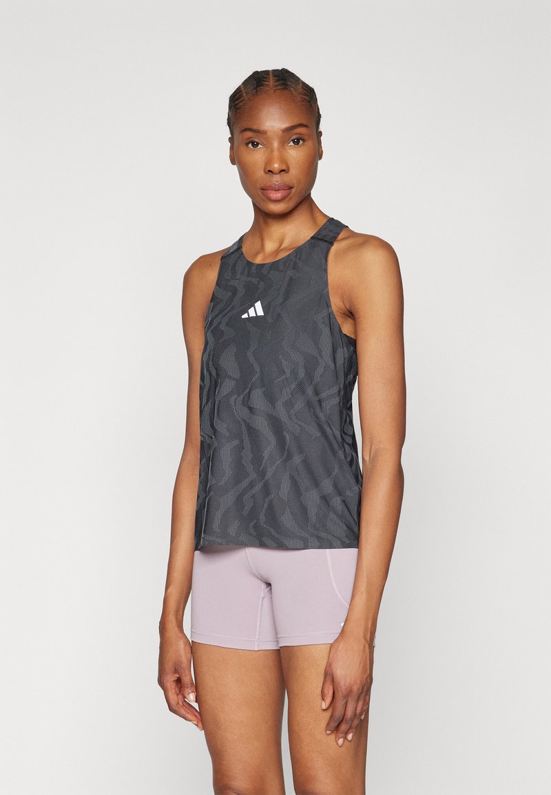 Canottiera sportiva grigia con motivo a onde testurizzato e logo bianco sul petto, abbinata a pantaloni corti aderenti rosa chiaro.