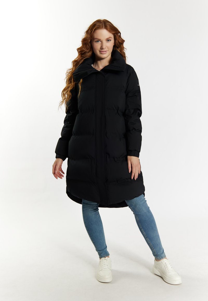 Schwarzer gepolsterter Mantel mit hohem Kragen, Frontreißverschluss und leichtem Glanz. Getragen über Jeans und weißen Sneakers. Glatte Oberflächenstruktur.