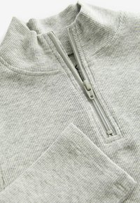 Lysegrå quarter-zip pullover lavet af ribbet stof. Har en forhøjet krave, lynlås-lukning og forstærkede sømme. Glat tekstur.