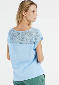 Lichtblauw kortemouwtop met een kanten ontwerp over de rug, met een ontspannen pasvorm en een ronde hals. Zachte textuur.