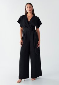 Črni kombinezon s širokimi hlačnicami in kratkimi krilastimi rokavi, z ovojnim dizajnom in pasom v pasu. Gladek tekstura in minimalističen slog.