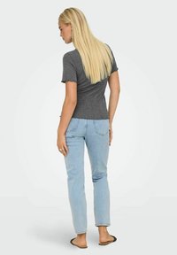 Grå kort�ærmet top med bølgede kanter, parret med lyseblå lige ben jeans. Modellen står med ryggen til, iført flade sandaler.