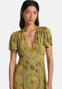 Πράσινο φόρεμα με κοντά μανίκια με βολάν, διακοσμημένο με σχέδιο φοινικόδεντρου και αστερία σε πορτοκαλί και κίτρινο. Σχεδιασμός με λαιμόκοψη V, ελαφρύ ύφασμα.