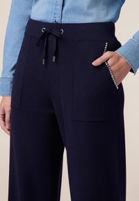 Pantaloni blu navy con vita regolabile mediante cordoncino, dotati di due tasche frontali e di un'applicazione di strass decorativi lungo il bordo delle tasche.