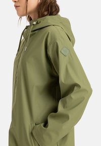 Olive green waterproof jacket with a hood, featuring a front zipper, adjustable drawstrings, and a square logo patch on the sleeve.