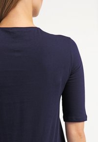 Mörkblå, kortärmad topp med rundad halsringning, tillverkad av mjukt och slätt material. Bakdesignen har minimala sömmar för en stilren look.