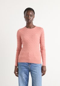 Pulover din bumbac moale de culoare roz, cu un model tricotat în cablu, având un guler rotund și mâneci lungi. Detaliu discret cu logo pe partea stângă a pieptului.