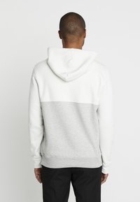 Sudadera con capucha que presenta una sección superior blanca y una sección inferior gris. Confeccionada en una tela suave con puños y dobladillo acanalados. Diseño minimalista.