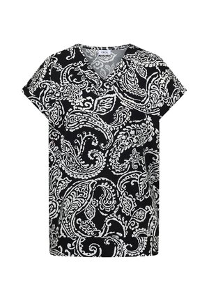 Femme portant une chemise à manches courtes à motif cachemire noir et blanc et un jean bleu, vue de dos et regardant sur le côté.