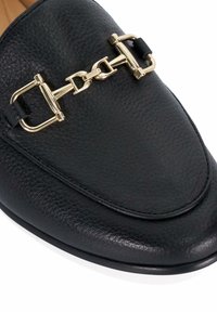 Zwarte leren loafers met een ronde neus, voorzien van een gouden metalen kettingaccent en stikdetails langs de rand.