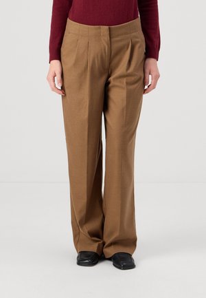 Pantalons plissés marron en tissu doux, avec un design à jambe large et une texture lisse. Portés avec des chaussures noires.