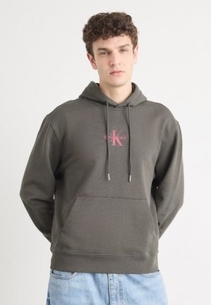 Donker olijfgroene hoodie van zachte stof met een voorzak, een capuchon met trekkoord en een roze Calvin Klein-logo op de borst.