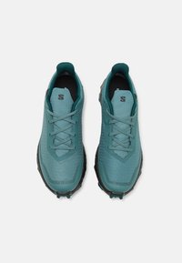 Turkusowe buty sportowe z teksturowaną cholewką, z czarną podeszwą, sznurowanym zapięciem i małym logo na języku.