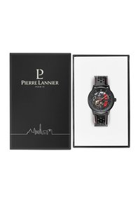 Montre noire avec un cadran transparent, accents rouges et dorés, sur un bracelet en cuir perforé noir, présentée dans une boîte noire avec logo.
