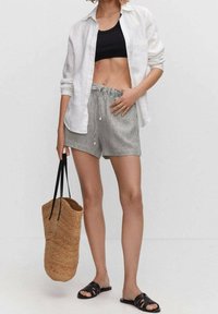 Musta crop-top, pitkä valkoinen pellavapaita, raidalliset shortsit, mustat liukusandaalit ja kudottu olkikassi mustilla kahvoilla.