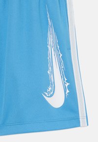 Pantalones cortos deportivos azules hechos de tela de malla texturizada, que presentan un gran logo de Nike en blanco con acentos afilados y angulares, además de franjas blancas a los lados.