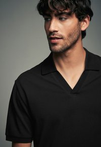 Polo nero con collo a V e maniche corte. Realizzato in tessuto texturizzato, presenta un design pulito e minimalista.