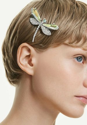 Kurzhaarige Person mit heller Haut und blauen Augen, die eine haarspange in Form einer Libelle mit durchscheinenden, glitzernden Flügeln trägt.