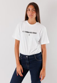 T-shirt bianca in cotone con il testo "H. I. / HUMAN INTELLIGENCE" in nero, abbinata a jeans a vita alta blu scuro. Design semplice e casual.