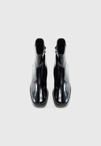 Bottines en cuir verni noir avec une finition lisse, fermeture éclair sur le côté et couture minimale, présentant un bout rond et une semelle durable.