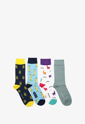 Quatre chaussettes colorées à motifs, posées à plat, présentant des ondes sonores jaunes, des suricates, des lamas multicolores et des pois blancs sur fond gris.
