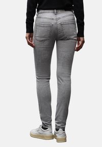 Jeans ajustados grises con bolsillos traseros, que presentan una textura suave. Combinados con una camiseta negra y zapatillas blancas. Detalle de costuras claras.