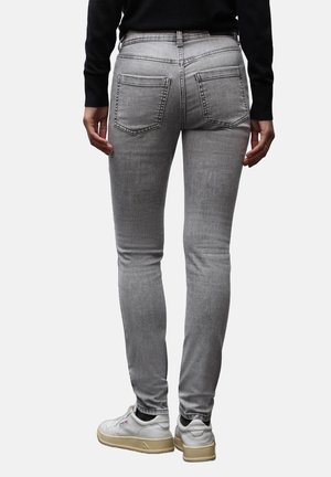 Grå skinny jeans med baglommer, der har en glat tekstur. Båret med en sort top og hvide sneakers. Tydeligt syning detalje.