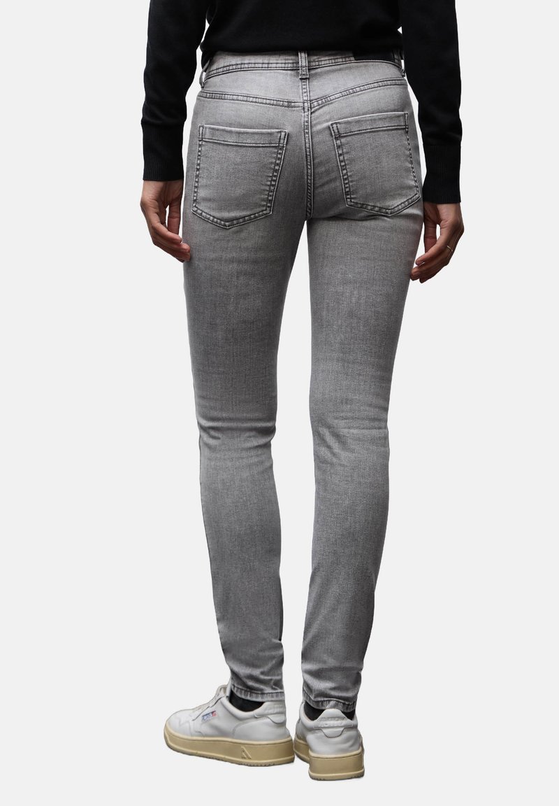 Jeans ajustados grises con bolsillos traseros, que presentan una textura suave. Combinados con una camiseta negra y zapatillas blancas. Detalle de costuras claras.