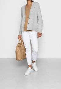 Szary kardigan z guzikami, beżowa bluzka z dekoltem w serek, białe krótkie dżinsy i białe trampki. Trzyma beżową torbę na ramię z detalem na sznurowadła.