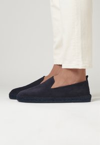 Espadrilles de ante azul marino con suela de yute trenzada, que presentan un diseño fácil de poner y una puntera redondeada. Los zapatos tienen aberturas en los laterales para mayor transpirabilidad.