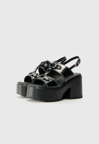 Black platform sandals with a glossy finish, featuring an open toe, adjustable buckle strap, and decorative metallic accents.