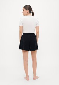 Vit kortärmad topp och svarta shorts, tillverkade av mjukt material. Shorts har ett elastiskt midjeband och en utsvängd design.
