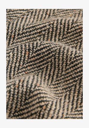 Tkanina s tkaným vzorem rybí kosti má černou a krémovou barvu s jemnými pomerančovými skvrnami; texturovaný povrch s jemnými vlákny.