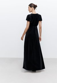 Abito lungo in velluto nero con maniche corte a sbuffo, scollatura rotonda e dettaglio in vita con fiocco. Tessuto liscio, silhouette elegante.