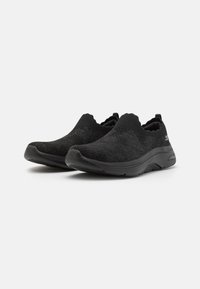 Fekete slip-on cipők kötött felsőrésszel, lekerekített orral, elasztikus gallérral és rugalmas gumi talppal. Minimalista dizájn textúrázott részletekkel.