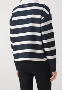 Suéter a rayas en azul marino y blanco con cuello. Presenta un diseño corto y un logo en la parte posterior. Tejido suave y texturizado. Mangas sin costuras.