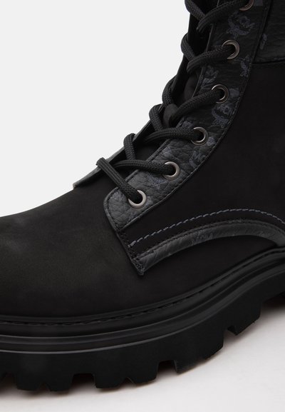 Botte noire en cuir à lacets avec panneaux latéraux texturés, œillets métalliques, semelle épaisse crantée et logos de marque embossés subtils.