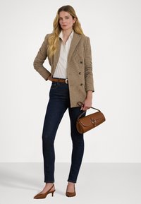 Dubbelzijdige houndstooth blazer in bruin, witte blouse, donkerdenim skinny jeans, bruine riem en schoudertas, met puntige bruine hakken.