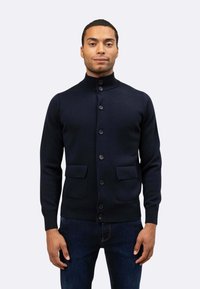 Cardigan in lana blu navy con colletto alto, sette bottoni sul davanti e due tasche a toppa in vita. Texture liscia e design aderente.