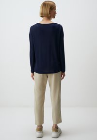 Navyblaues Langarmhemd mit lockerer Passform, kombiniert mit hellbeigen Hosen. Das Outfit zeichnet sich durch ein schlichtes Design und eine weiche Stoffstruktur aus.