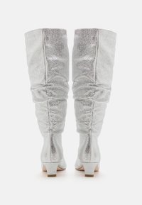 Bottes argentées au-dessus du genou avec une texture brillante et pailletée ; design froncé ; talons blocs ; intérieur lisse ; bout arrondi.