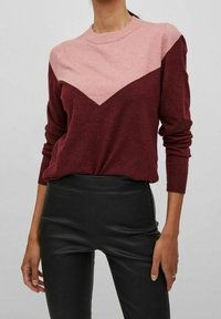 Burgundy och blush färgblockerad tröja med en chevronmönster, rund halsringning och långa ärmar, tillverkad av mjukt stickat material.