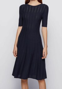 Marinblå stickad klänning med korta ärmar. Har vertikala ränder och en utsvängd nederdel. Tillverkad av textil med en struktur och öppna vävsektioner.