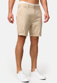 Beige cargo shorts med optrukne manchetter, lavet af tekstureret stof, med forlommer og knaplukning. Bæres med hvide sneakers.