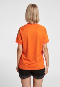 Oranje sportshirt met een textuurafwerking en zwarte shorts. Heeft raglanmouwen en minimale grijze accenten op de schouders.