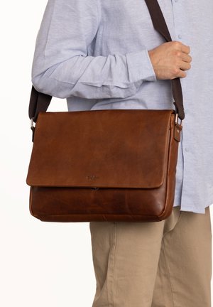 Sac messenger en cuir marron avec fermeture à rabat et bandoulière en tissu réglable. Présente une texture lisse et un discret logo à l'avant.