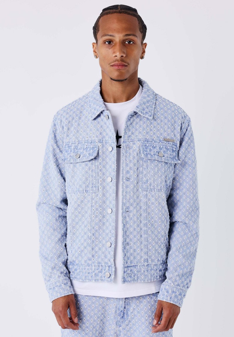 Lichtblauwe spijkerjas met een gestructureerd diamantenpatroon, twee borstzakken en metalen knopen. Voorzien van een kraag en lange mouwen.